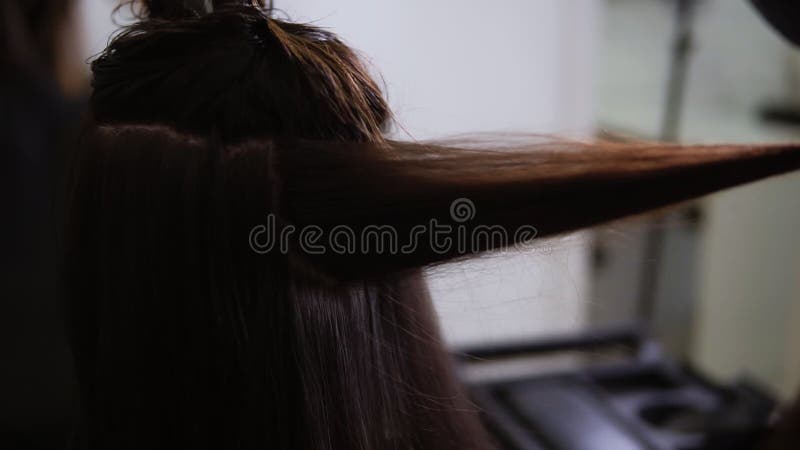 Stängning av hårfrisörhänder som torkar långa mörka hår av kvinnor som sitter i sallonstol Hårborttagare med fläkt