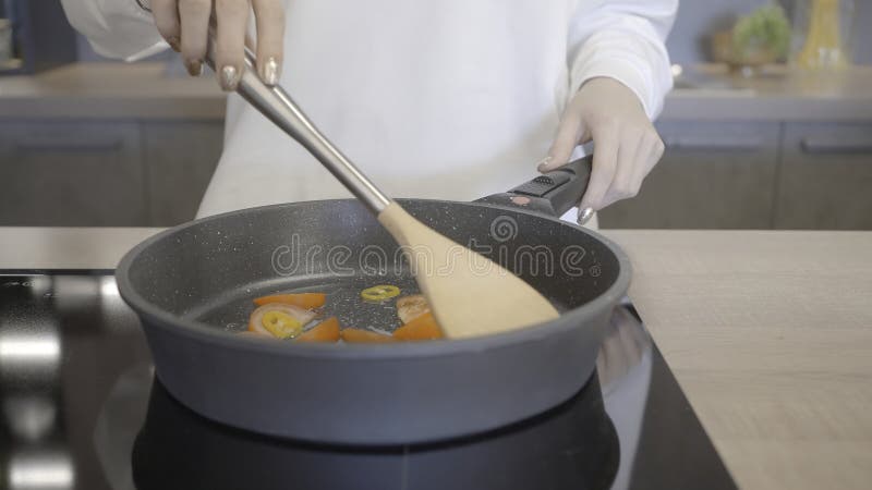 Close-up of woman cooking in new frying pan. Action. Roasting vegetables on new modern model of frying pan. Cooking healthy food in new frying pan. Close-up of woman cooking in new frying pan. Action. Roasting vegetables on new modern model of frying pan. Cooking healthy food in new frying pan.