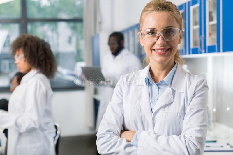 Stående av att le kvinnan i det vita laget och skyddande glasögon i det moderna laboratoriumet, kvinnlig forskare Over Busy royaltyfri fotografi