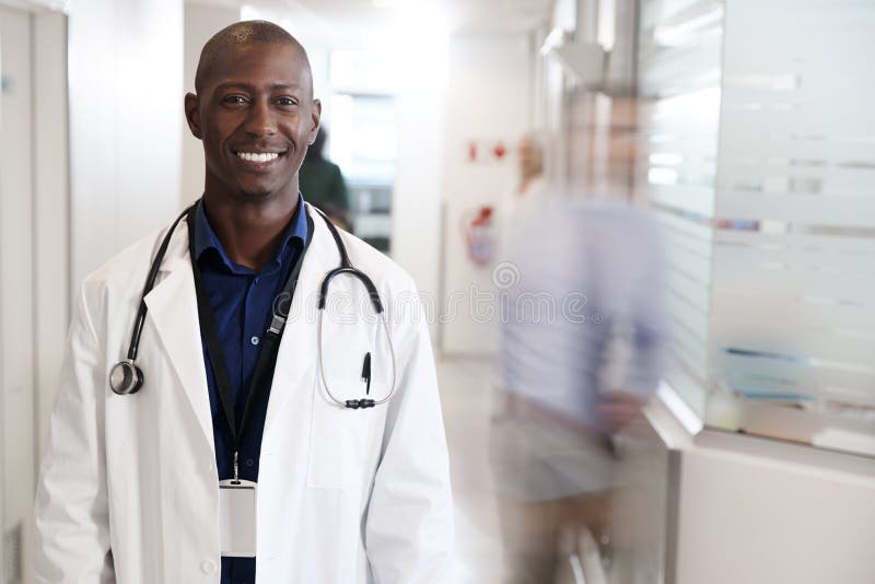 Stående av att le manlig doktor Wearing White Coat med stetoskopet i upptagen sjukhuskorridor royaltyfria bilder Stående av att le manlig doktor Wearing White Coat med stetoskopet i upptagen sjukhuskorridor royaltyfria bilder
