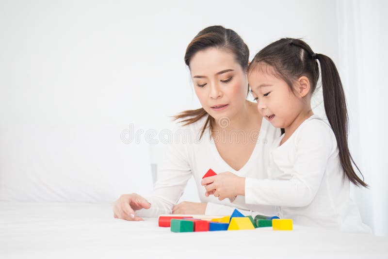 Stående av den asiatiska lilla gulliga flickan som spelar färgrika kvarter med hennes moder över vit bakgrund arkivbild