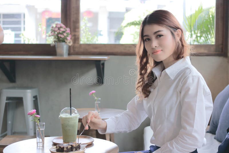 Stående av den attraktiva unga asiatiska kvinnan som äter nisseefterrätten med gaffeln i kaffekafé royaltyfri foto Stående av den attraktiva unga asiatiska kvinnan som äter nisseefterrätten med gaffeln i kaffekafé royaltyfri foto