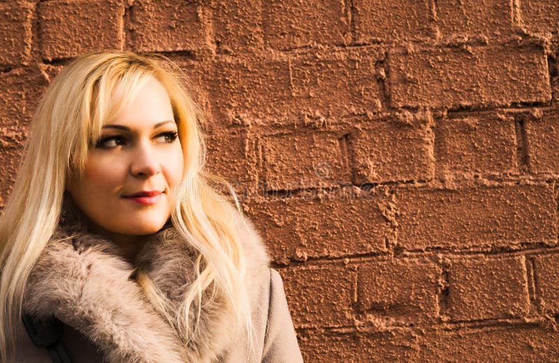 Stående av den blonda flickan i varmt lag över en tegelstenvägg royaltyfri fotografi Stående av den blonda flickan i varmt lag över en tegelstenvägg royaltyfri fotografi