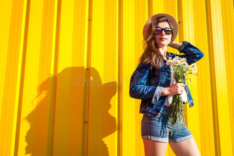 Stående av den bärande exponeringsglas och hatten för hipsterflicka med blommor mot gul bakgrund Sommardräkt Mode avstånd royaltyfria bilder Stående av den bärande exponeringsglas och hatten för hipsterflicka med blommor mot gul bakgrund Sommardräkt Mode avstånd royaltyfria bilder
