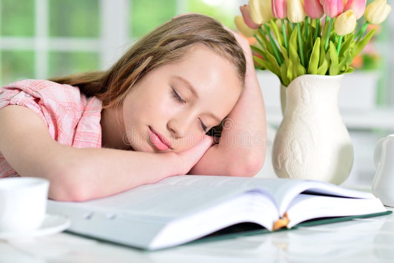 Stående av den gulliga flickan som sover på den öppnade boken arkivfoto