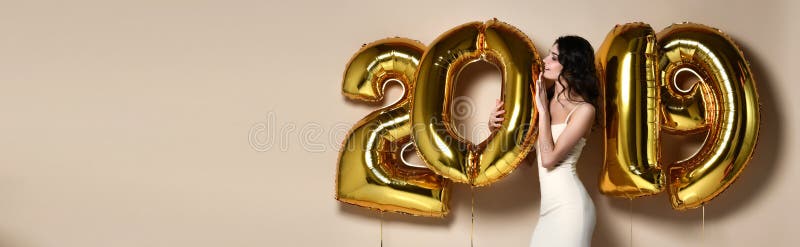 Stående av den härliga le flickan i skinande guld- klänning som kastar konfettier och att ha gyckel med guld- 2018 ballonger på b arkivfoto Stående av den härliga le flickan i skinande guld- klänning som kastar konfettier och att ha gyckel med guld- 2018 ballonger på b arkivfoto