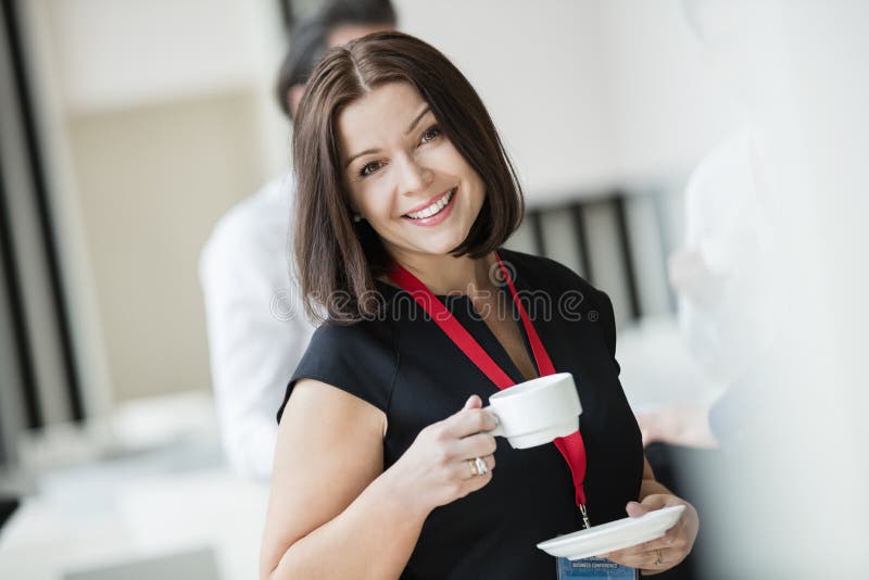 Stående av den hållande kaffekoppen för lycklig affärskvinna i seminariumkorridor arkivfoto