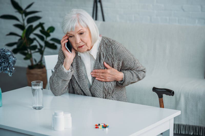 stående av den höga kvinnan med hjärtaknip som talar på smartphonen på tabellen med mediciner royaltyfri bild stående av den höga kvinnan med hjärtaknip som talar på smartphonen på tabellen med mediciner royaltyfri bild