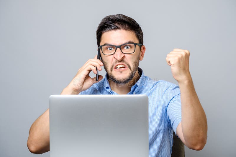 Portrait of angry young man screaming on his mobile phone over gray background. Portrait of angry young man screaming on his mobile phone over gray background