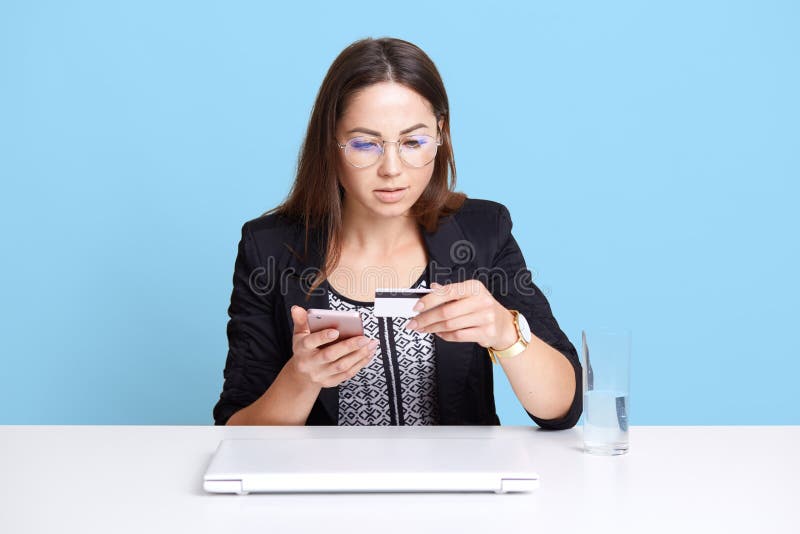 Stående av den koncentrerade yrkesmässiga affärskvinnan som använder mobiltelefonen, och kreditkorten på hennes arbete och att si arkivfoton Stående av den koncentrerade yrkesmässiga affärskvinnan som använder mobiltelefonen, och kreditkorten på hennes arbete och att si arkivfoton