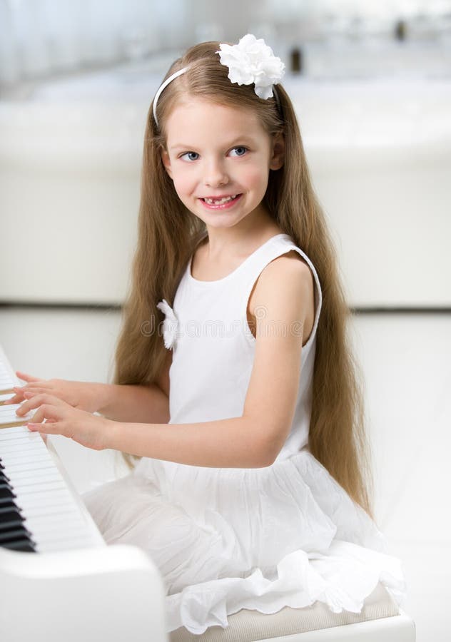 Stående av den lilla pianisten i den vita klänningen som spelar pianot arkivbild Stående av den lilla pianisten i den vita klänningen som spelar pianot arkivbild