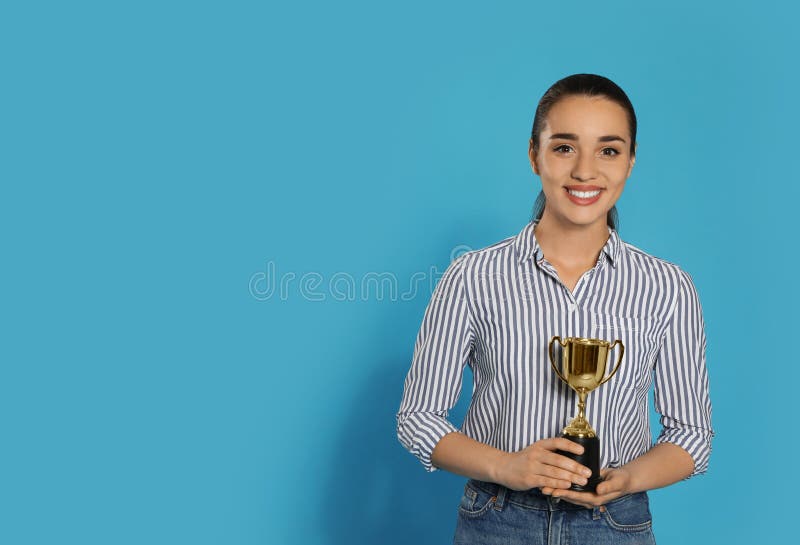 Stående av den lyckliga unga kvinnan med den guld- trofékoppen på blå bakgrund, utrymme för royaltyfri bild Stående av den lyckliga unga kvinnan med den guld- trofékoppen på blå bakgrund, utrymme för royaltyfri bild
