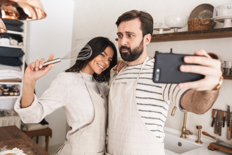 Stående av den optimistiska parman- och kvinna30-tal som bär förkläden som tar selfiefotoet, medan laga mat hemma royaltyfria bilder Stående av den optimistiska parman- och kvinna30-tal som bär förkläden som tar selfiefotoet, medan laga mat hemma royaltyfria bilder