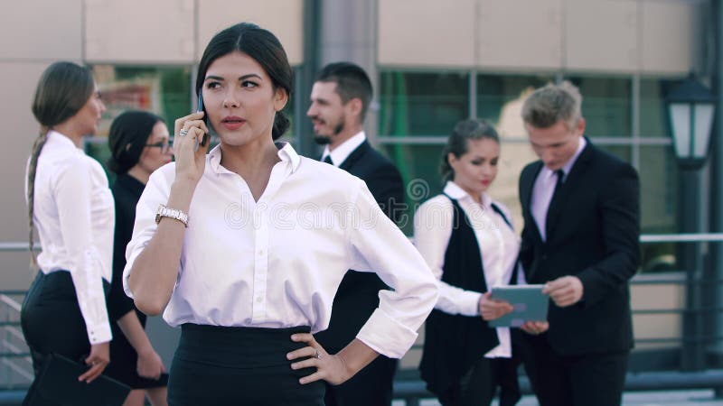 Stående av den stilfulla unga affärskvinnan som talar på telefonen och hennes Smart-seende coworkers som står och talar till stock video