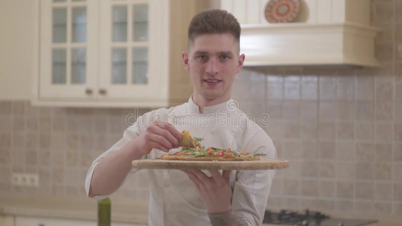 Stående av den stiliga le unga mannen som rymmer träplattan med pizzaslut upp Begrepp av matförberedelsen