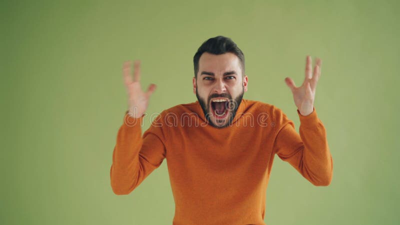 Stående av den stressade unga mannen som skriker lyfta armar på grön bakgrund