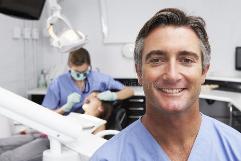 Stående av den tandsköterskaWith Dentist Examining patienten i bakgrund arkivfoton Stående av den tandsköterskaWith Dentist Examining patienten i bakgrund arkivfoton