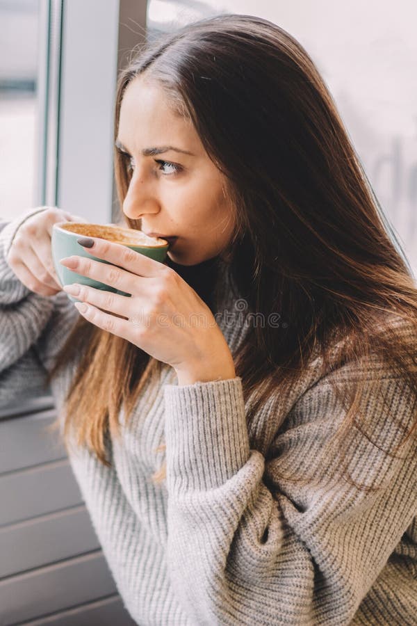 stående av den unga härliga gulliga brunettflickan i grå tröja som dricker kaffe arkivbilder stående av den unga härliga gulliga brunettflickan i grå tröja som dricker kaffe arkivbilder