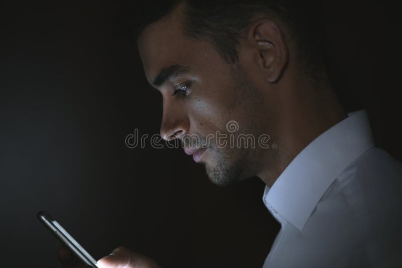 Stående av den unga stiliga mannen som använder den smarta telefonen i hand på mörk bakgrund royaltyfri bild Stående av den unga stiliga mannen som använder den smarta telefonen i hand på mörk bakgrund royaltyfri bild