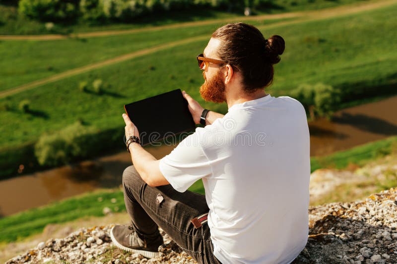 Stående av den unga stiliga skäggiga hipstermannen som utanför använder en minnestavla arkivbild Stående av den unga stiliga skäggiga hipstermannen som utanför använder en minnestavla arkivbild
