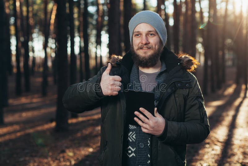 Stående av den vuxna mannen som går i pinjeskogen med den digitala minnestavlan royaltyfria bilder Stående av den vuxna mannen som går i pinjeskogen med den digitala minnestavlan royaltyfria bilder
