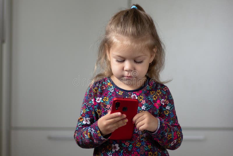 Stående av det gulliga och attraktiva barnet som ser mobiltelefonen och rymmer den i händer arkivbilder