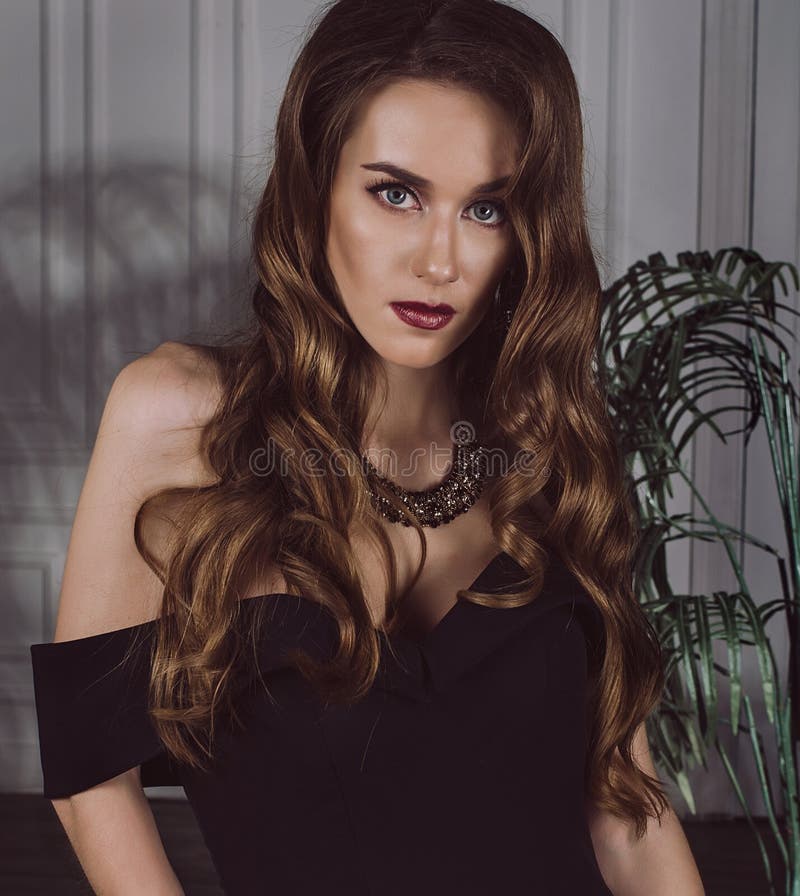 Stående av en attraktiv stilfull sexig brunhårig kvinna i en svart klänning med öppna skuldror i studion Nära övre Fashi royaltyfri foto Stående av en attraktiv stilfull sexig brunhårig kvinna i en svart klänning med öppna skuldror i studion Nära övre Fashi royaltyfri foto