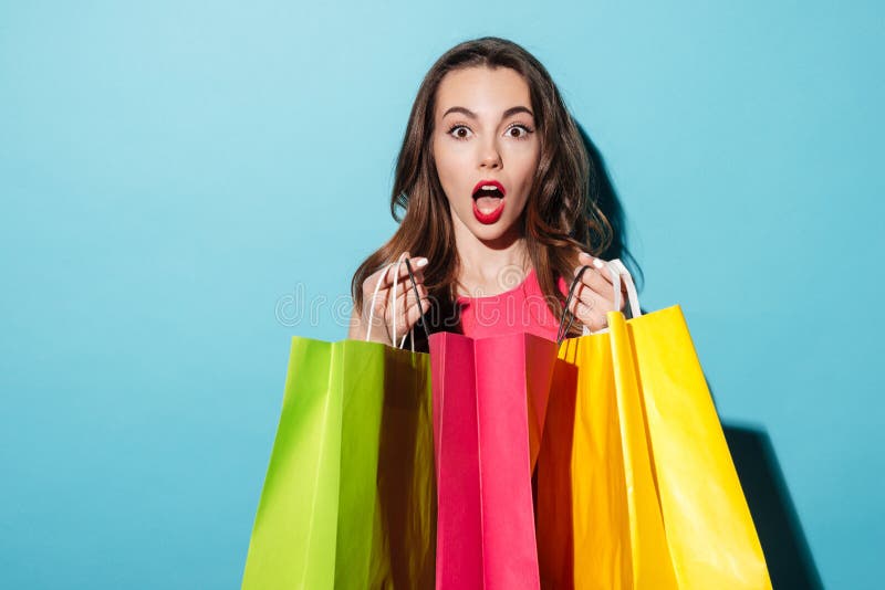 Stående av en chockad nätt flicka som rymmer färgrika shoppingpåsar royaltyfri bild Stående av en chockad nätt flicka som rymmer färgrika shoppingpåsar royaltyfri bild