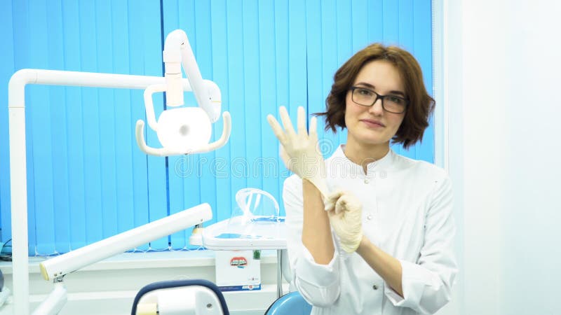 Stående av en doktor för härlig ung kvinna som bär medicinska handskar Kvinnlig tand- assistent i exponeringsglas som sätter på h arkivbild Stående av en doktor för härlig ung kvinna som bär medicinska handskar Kvinnlig tand- assistent i exponeringsglas som sätter på h arkivbild