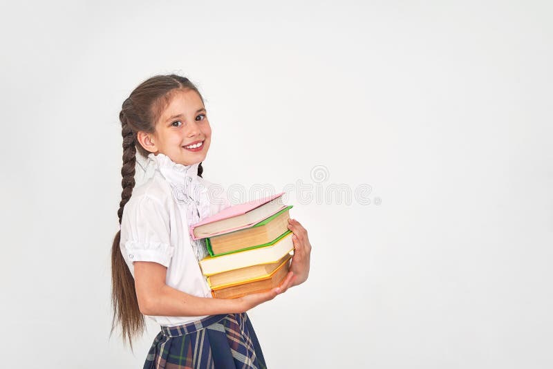 Stående av en härlig liten flickastudent med en ryggsäck och en bunt av böcker i hans händer som ler på en vit bakgrund arkivbilder Stående av en härlig liten flickastudent med en ryggsäck och en bunt av böcker i hans händer som ler på en vit bakgrund arkivbilder