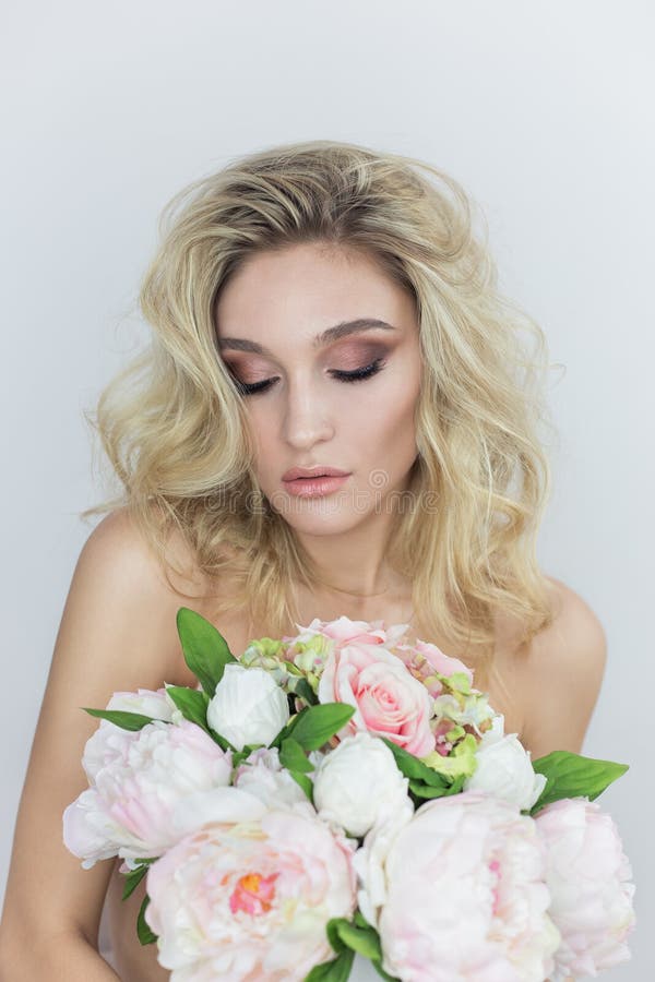 Stående av en härlig sexig ung kvinna med ljus makeup med kala skuldror som rymmer en stor bukett i händer på en vit backgr royaltyfri fotografi Stående av en härlig sexig ung kvinna med ljus makeup med kala skuldror som rymmer en stor bukett i händer på en vit backgr royaltyfri fotografi