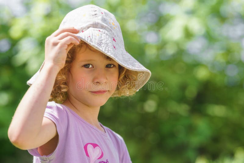 Stående av en liten caucasian flicka med en hatt som skyddar från den hårda solen Gr?n blurbakgrund arkivbilder Stående av en liten caucasian flicka med en hatt som skyddar från den hårda solen Gr?n blurbakgrund arkivbilder