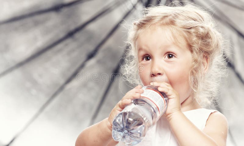 Stående av en rolig gullig liten flicka i en tillfällig klänning, drinkvatten, medan sitta i studio arkivbild Stående av en rolig gullig liten flicka i en tillfällig klänning, drinkvatten, medan sitta i studio arkivbild