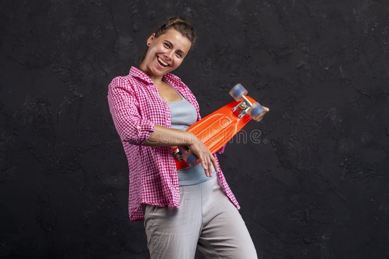 Stående av en trendig härlig ung flicka med en skateboard i händer arkivfoto Stående av en trendig härlig ung flicka med en skateboard i händer arkivfoto