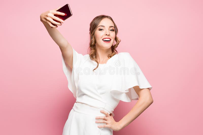 Stående av ett ungt attraktivt foto för kvinnadanandeselfie med smartphonen på en rosa bakgrund royaltyfria foton Stående av ett ungt attraktivt foto för kvinnadanandeselfie med smartphonen på en rosa bakgrund royaltyfria foton