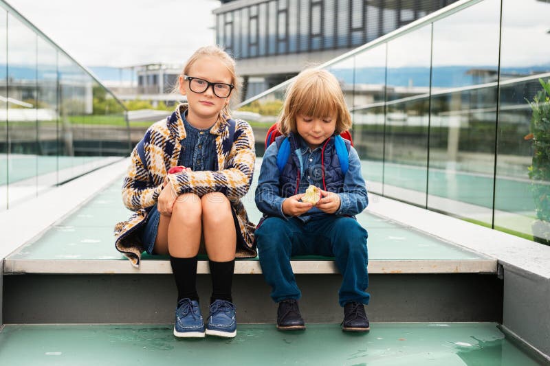 Cute kids with backpacks sitting on stairs next to school, wearing backpack, eating apples. Cute kids with backpacks sitting on stairs next to school, wearing backpack, eating apples