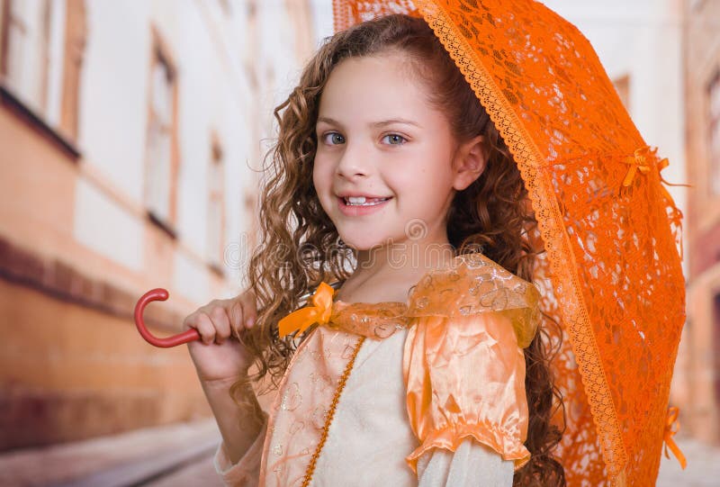 Stående av lilla flickan som bär en härligt kolonialt dräkt och innehav ett orange paraply i en suddig bakgrund fotografering för bildbyråer Stående av lilla flickan som bär en härligt kolonialt dräkt och innehav ett orange paraply i en suddig bakgrund fotografering för bildbyråer