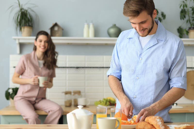 Stående av lyckliga unga par i pyjamas som tillsammans lagar mat i köket som hemma dricker orange fruktsaft i morgonen arkivfoton Stående av lyckliga unga par i pyjamas som tillsammans lagar mat i köket som hemma dricker orange fruktsaft i morgonen arkivfoton