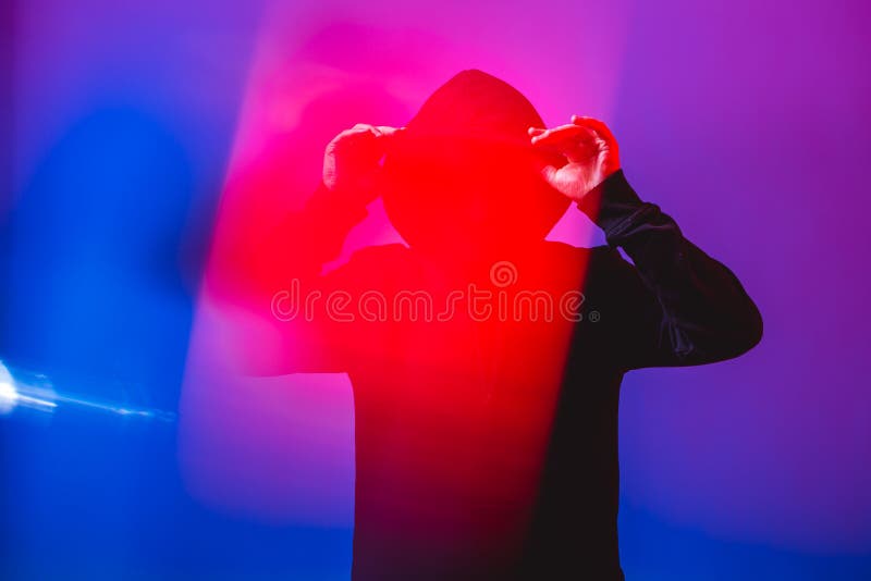 Stående av modemannen i en svart tröja med en huv och solglasögon i neonljus i studion arkivbild Stående av modemannen i en svart tröja med en huv och solglasögon i neonljus i studion arkivbild