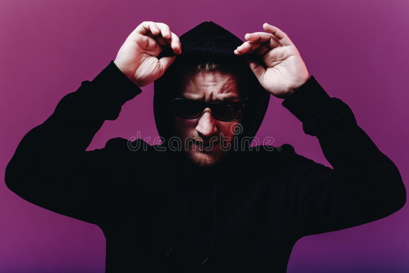 Stående av modemannen i en svart tröja med en huv och solglasögon i neonljus i studion royaltyfri foto Stående av modemannen i en svart tröja med en huv och solglasögon i neonljus i studion royaltyfri foto