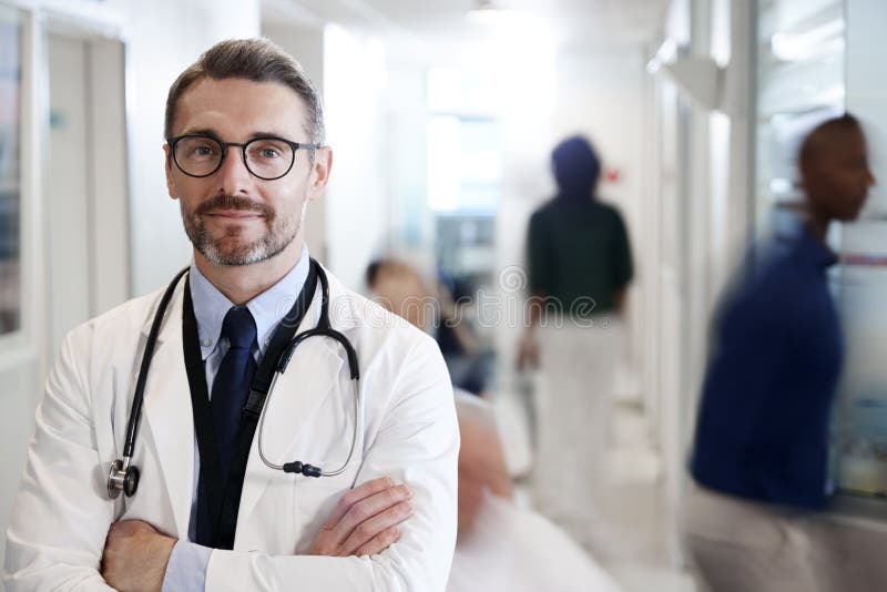Stående av mogen manlig doktor Wearing White Coat med stetoskopet i upptagen sjukhuskorridor arkivbilder Stående av mogen manlig doktor Wearing White Coat med stetoskopet i upptagen sjukhuskorridor arkivbilder