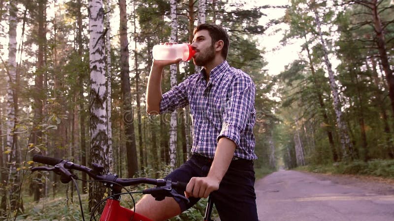 Stående av stiligt mansammanträde på cykeln och dricksvatten lager videofilmer