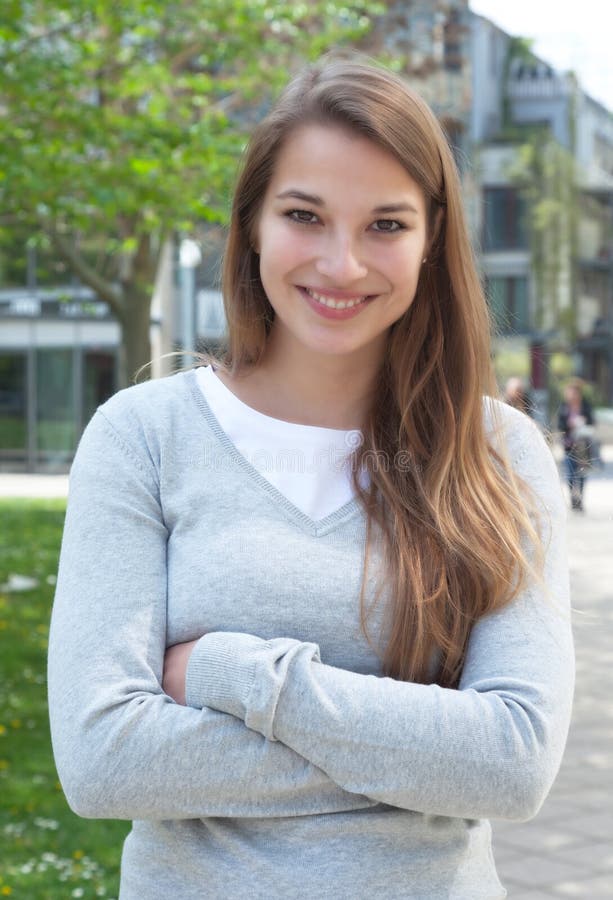 Stående ung kvinna med korsade armar i tillfällig kläder utanför arkivfoto Stående ung kvinna med korsade armar i tillfällig kläder utanför arkivfoto