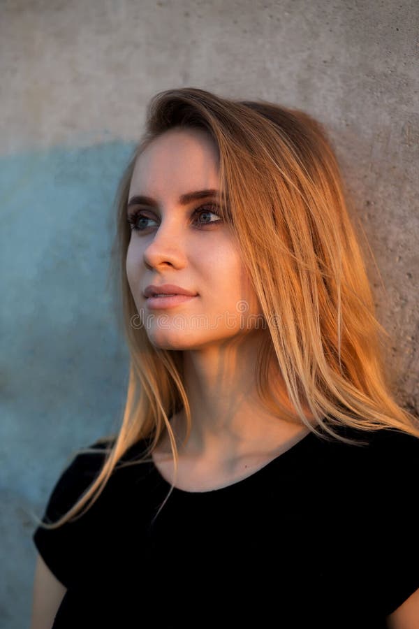 Stående åt sidan av den härliga blonda kvinnan i svart överkant nära väggen arkivbilder Stående åt sidan av den härliga blonda kvinnan i svart överkant nära väggen arkivbilder