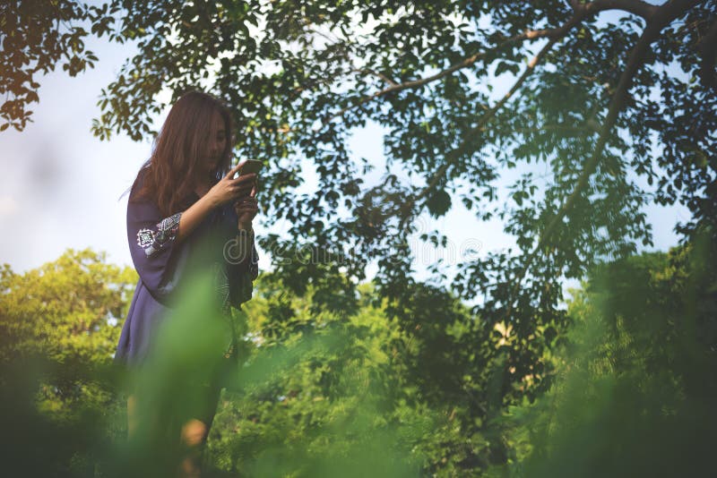 Ståendebild ett härligt asiatiskt kvinnaanseende och använda den smarta telefonen med den gröna naturen royaltyfri fotografi Ståendebild ett härligt asiatiskt kvinnaanseende och använda den smarta telefonen med den gröna naturen royaltyfri fotografi