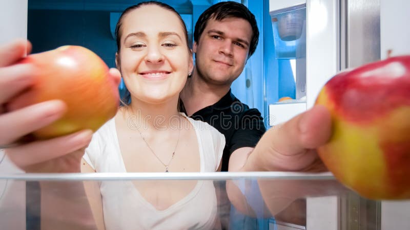Ståenden av att le barn kopplar ihop att ta äpplen från kylskåpet på natten royaltyfri bild Ståenden av att le barn kopplar ihop att ta äpplen från kylskåpet på natten royaltyfri bild