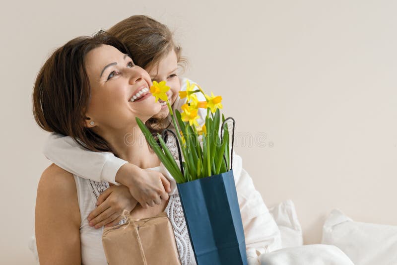 Ståenden av den lyckliga modern och lilla dottern som ler och omfamnar, flickan gratulerar hennes moder med buketten av blommor M royaltyfri foto Ståenden av den lyckliga modern och lilla dottern som ler och omfamnar, flickan gratulerar hennes moder med buketten av blommor M royaltyfri foto