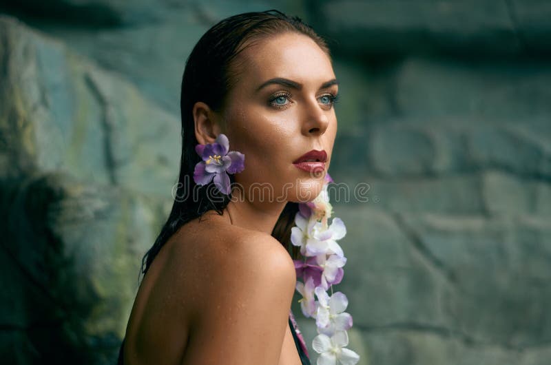 Ståenden av en attraktiv ung kvinna med örhängen i form av tropiska blommor mot vaggar fotografering för bildbyråer Ståenden av en attraktiv ung kvinna med örhängen i form av tropiska blommor mot vaggar fotografering för bildbyråer