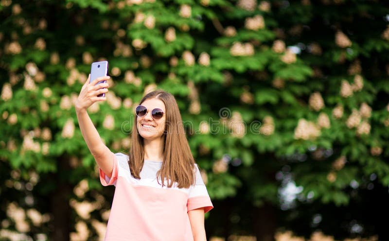 Ståenden av en härlig ung kvinna i solglasögon tar selfie med en smartphone arkivfoton Ståenden av en härlig ung kvinna i solglasögon tar selfie med en smartphone arkivfoton