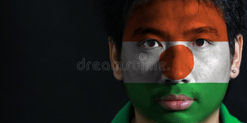 Ståenden av en man med flaggan av Niger målade på hans framsida på svart bakgrund arkivfoto Ståenden av en man med flaggan av Niger målade på hans framsida på svart bakgrund arkivfoto
